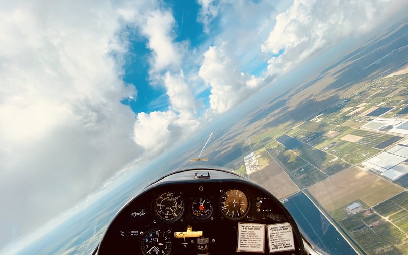 Cockpit view of a Miami Gliders sailplane over South Florida fields and cloudscape