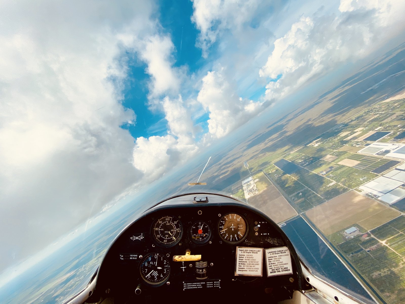 Glider cockpit instrument panel with towering clouds and farmland below
